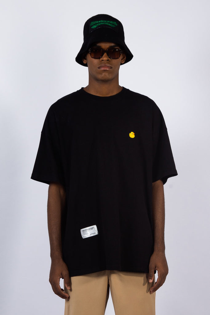 Mdel is wearing a t-shirt from Leblanc studios.  It is a black t-shirt with an orange ducm embroidery on the chest and white rectangular label near the bottom of the t-shirt.  Model is also wearing black sunglasses a black bucket hat.