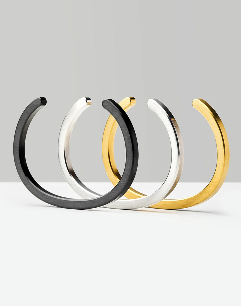 1 of 7 A black cuff, silver cuff and brass cuff aligned in a row with a gray background