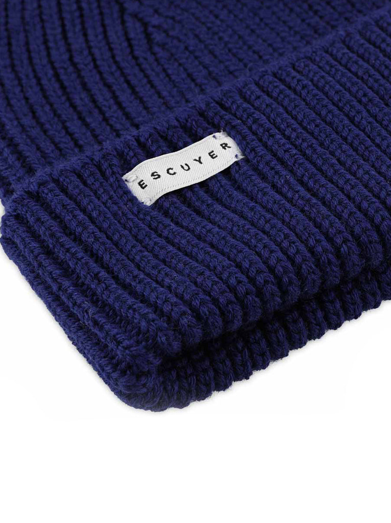 A close-up image of the Escuyer Blue ribbed beanie with a small Escuyer white label on the foldover, which can easily be removed.