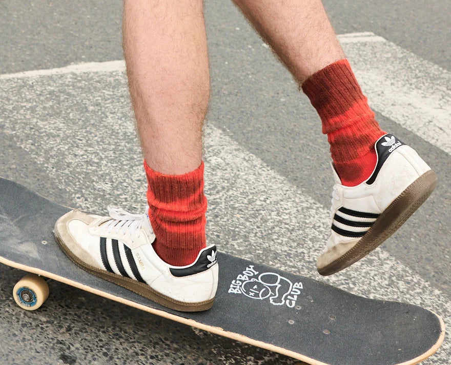 Close-up of skateboard with person wearing sneakers and Escuyer red tie-dye colored ribbed socks.