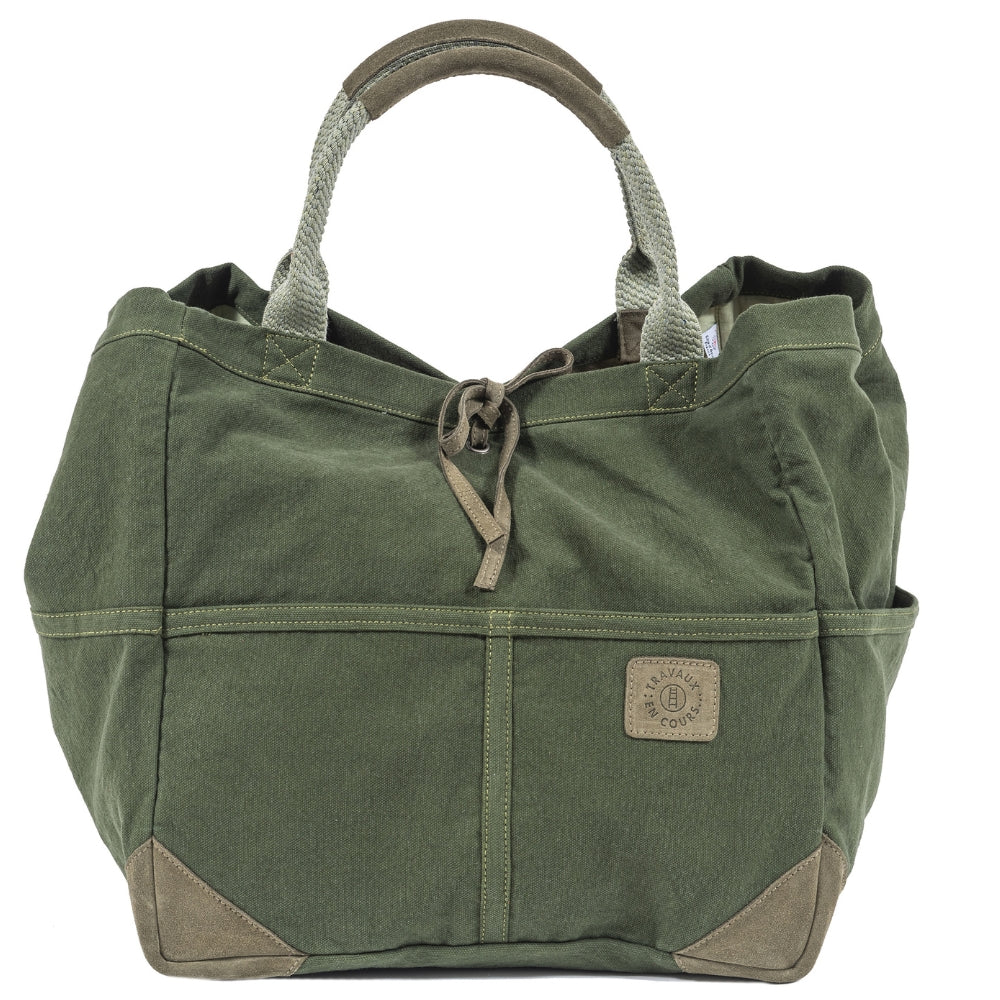 Front view of the green tote bag with two curved handles with leather trim.  Khaki green leather tie in the center of bag with khaki green logo patch on center right of bag.  Slide 2 of 4