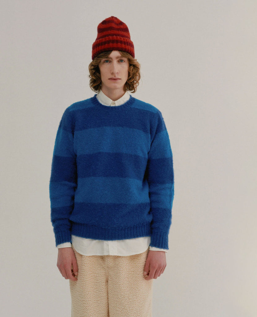 Person wearing a blue striped wool sweater and red striped beanie on a plain background