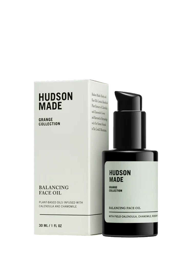 Hudson Made Grange Collection Balancing Face Oil box on the left "Plant based oils infused with calendula and chamomile" embossed in black print.  Black pump bottle is next to the box with the label mirroring the copy of the box. Slide 1 of 2