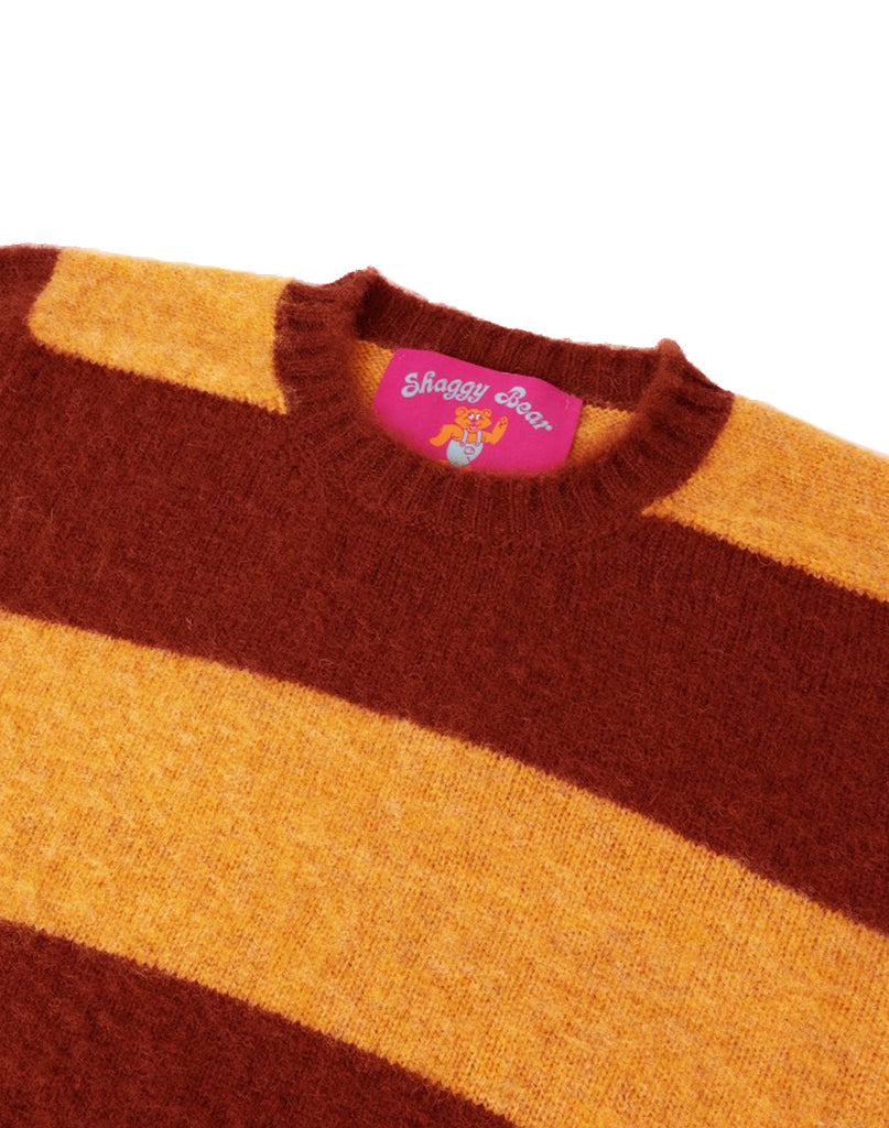 Photo 2 of 2. Close-up of a brown and orange striped sweater with a brand label in pink "Shaggy Bear" on a white background