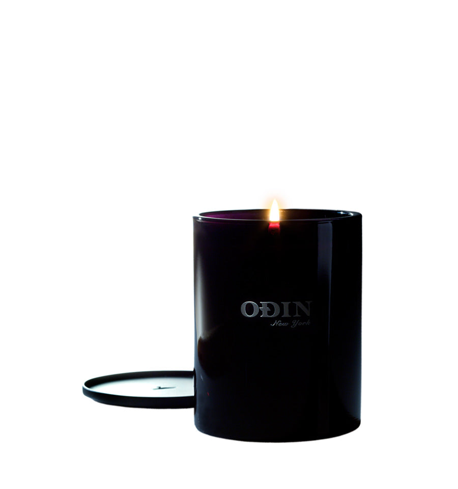 02 Owari votive size candle lit with Odin New York printed on the outside of the black vessel.  black Metal lid is shown next to the candle.